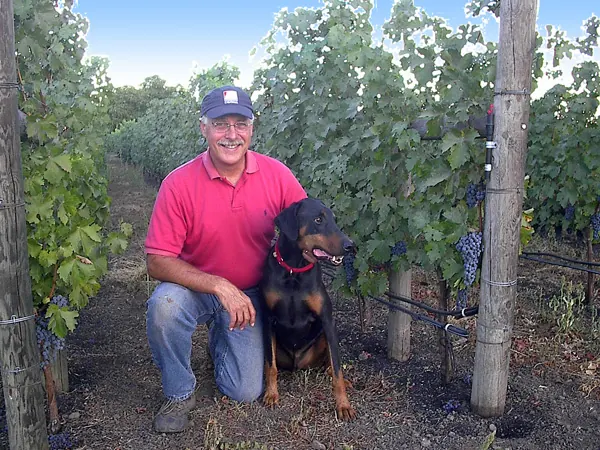 Randle Johnson kneeling in the vineyard with his dog Rhette