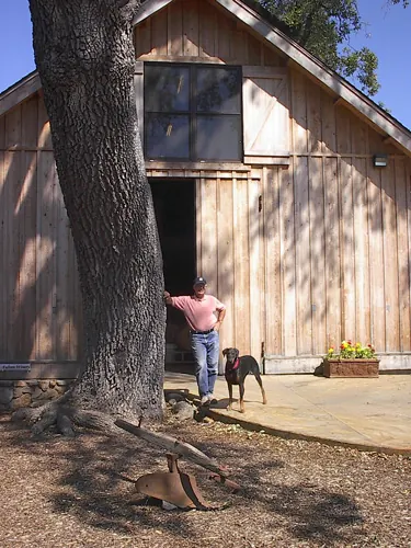 Randle Johnson and his dog outside the winery barn under an oak tree
